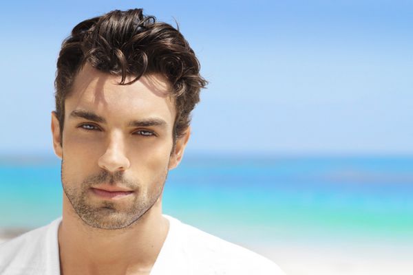 مرد جوان خوش تیپ در سفید سفارشی در مقابل پس زمینه ساحل روشن