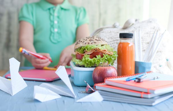 ناهار مدرسه در جعبه و آب با میوه در یک پس زمینه سبز و کتاب در دست یک دختر نان تست و آب در یک بطری فضای آزاد برای متن فضای کپی کنید