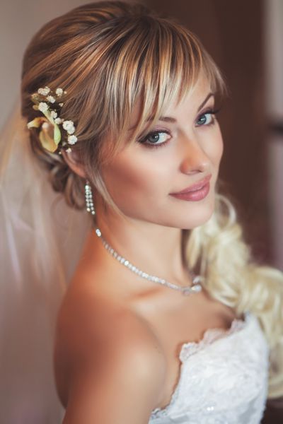 دختر زیبا عروس مبارک در لباس عروسی سفید با مدل موهای و آرایش روشن در انتظار داماد خانم رمانتیک در لباس عروسی و گل در مو آماده نهایی برای عروسی است