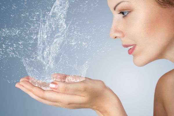 زن جوان او صورت و دستها را با آب تمیز شستشو در صبح