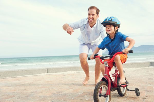 پدر و پسر یادگیری دوچرخه سواری در ساحل لذت بردن با هم