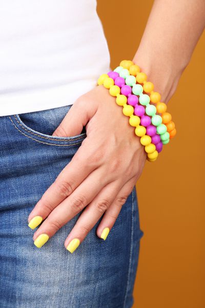 زن با ناخن شیک و رنگارنگ نزدیک در پس زمینه رنگی
