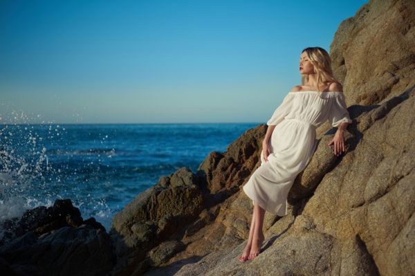 خانم زیبا در لباس سفید در ساحل سنگی