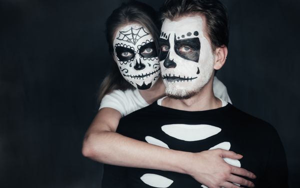 زن و شوهر در عشق با آرایش جمجمه تیره در پس زمینه سیاه و سفید هنر چهره هالووین