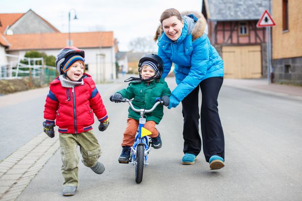 مادر جوان پسر 2 ساله خود را آموزش می دهد تا در خارج از منزل دوچرخه سواری کند یکی دیگر از بچه های برادر در کنار هم