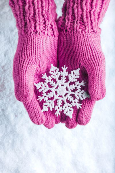 زن در دستکش های نازک صورتی سبک با برف ریزه ای فوق العاده شیک در پس زمینه سفید برفی دست دارد مفهوم زمستان و کریسمس