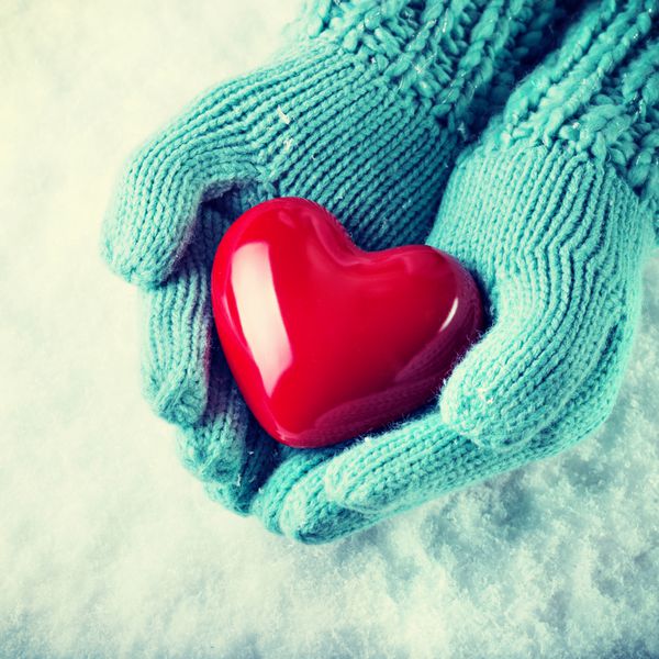 دستان زن در دستکش های چاق و چرب نازک یک قلب قرمز براق را در پس زمینه ی برف نگه می دارند عشق و مفهوم سنت فیلتر نمایش مشخصات عمومی