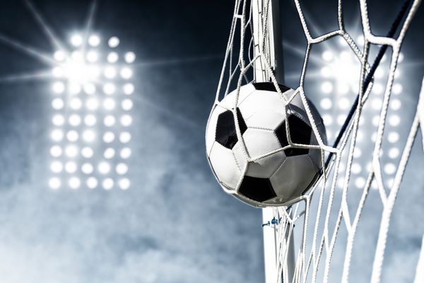 توپ فوتبال در شبکه هدف با چراغ استادیوم در پس زمینه