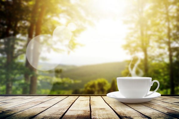 جام با چای روی میز روی چشم انداز کوهستانی با نور خورشید پس زمینه زیبایی طبیعت