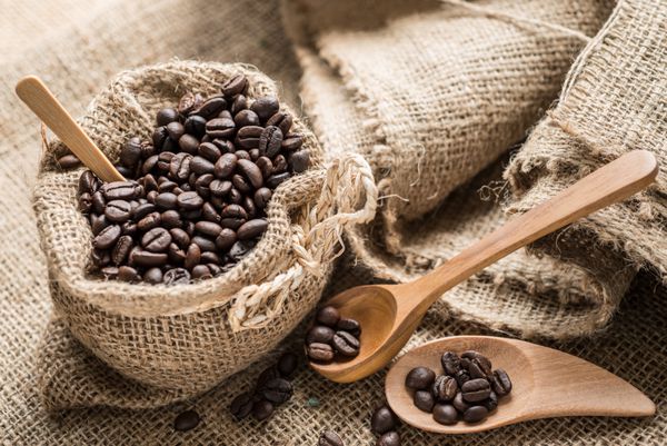 دانه های قهوه در کیسه های قهوه ساخته شده از خاکستری در سطح کیسه