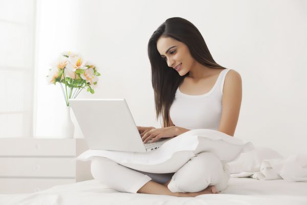زن جوان با استفاده از لپ تاپ در رختخواب