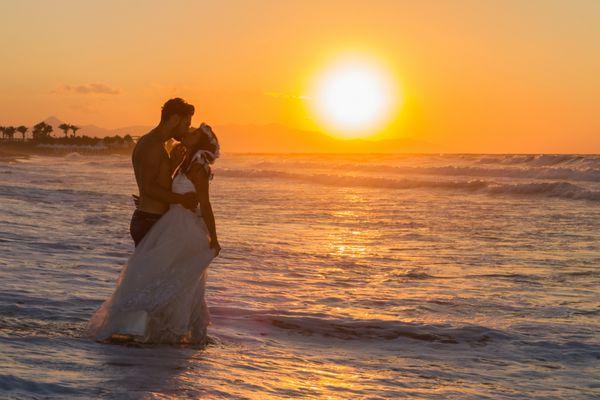 فقط زوج جوان در ساحل ازدواج می کنند لذت بردن از غروب خفیف پوشیدن لباس عروسی و شورت راه رفتن پابرهنه خیس شدن اذیت کردن و بوسیدن یکدیگر