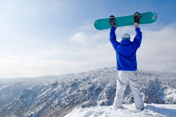 دید عقب از ورزشکار با اسنوبرد ایستاده در بالای کوه