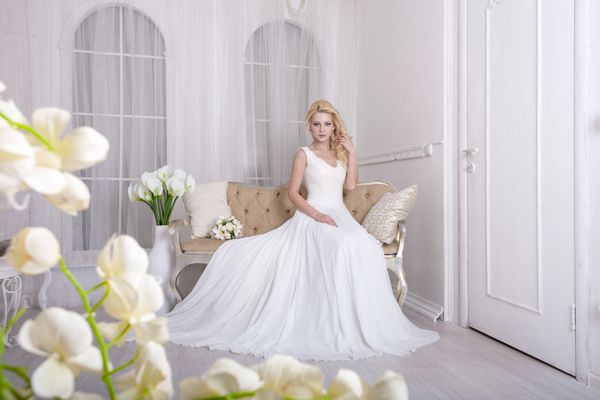 عروس زیبا بر روی نیمکت پرنعمت نشسته است لباسش حلق آویز شده روی زمین