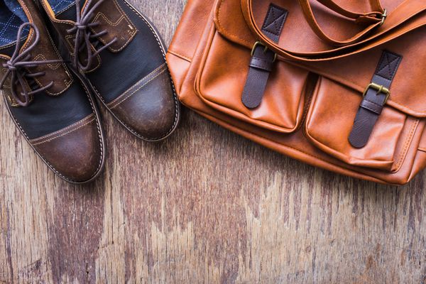 لوازم جانبی مردانه با کیسه های چرم قهوه ای و کفش های قهوه ای تخت نمایش بالا در زمینه های چوبی