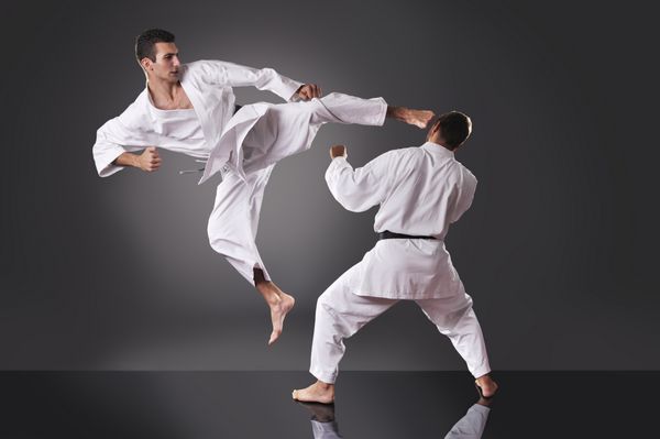 دو کاراته مرد جوان خوش تیپ که در پس زمینه خاکستری می جنگند