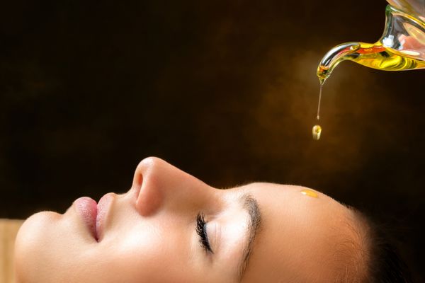 ماکرو نزدیک پرتره زن جوان در جلسه ماساژ ayurvedic با روغن های معطر چکیدن روی صورت