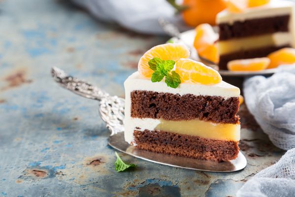 قطعه ای از کیک شکلاتی خوشمزه با ماندارین نارنگی مربا پوشیده شده با کرم پنیر در پس زمینه زرد آلو فلزی قدیمی است تمرکز انتخابی