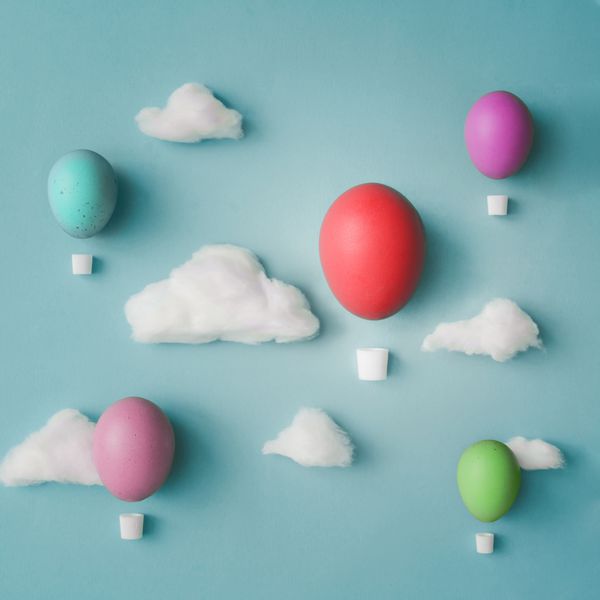 بالن های هوا ساخته شده از تخم مرغ عید پاک تزئین شده با ابرهای پنبه در پس زمینه روشن آبی تختخواب مفهوم خلاقانه