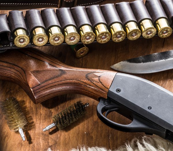 تجهیزات شکار تفنگ ساچمهای پمپ کارتریج شکار 12 میلیمتری و چاقو شکار بر روی میز چوبی