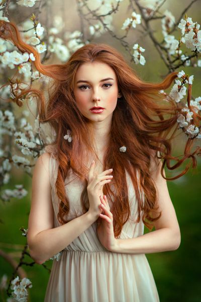 بهار دختر خوشگل رمانتیک قرمز مواج ایستاده در باغ شکوفه مدل جوان به دنبال دوربین است