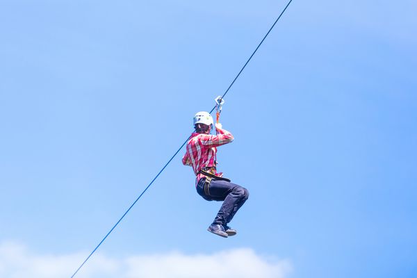 مرد جوان در zipline در برابر آسمان ابری در تابستان