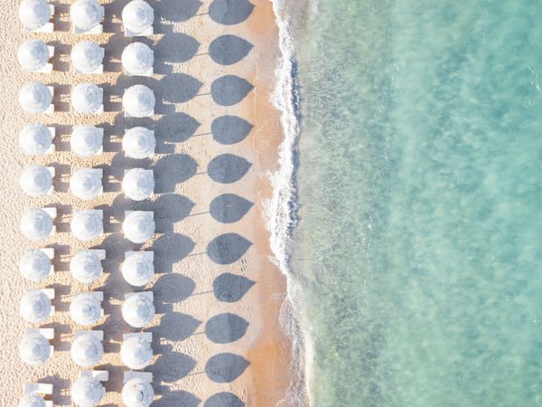 منظره هوایی از ساحل شگفت انگیز با چتر سفید و دریای فیروزه در غروب آفتاب دریای مدیترانه ساردینیا ایتالیا