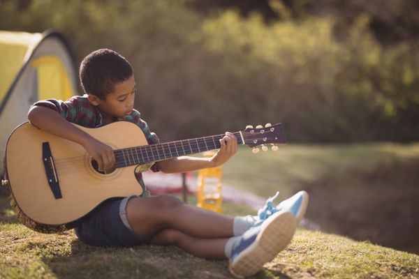 پرتره از گیتار پسر خندان در پارک در یک روز آفتابی
