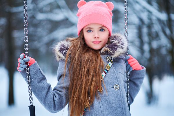 دختر کوچک جذاب در نوسان در زمستان برفی