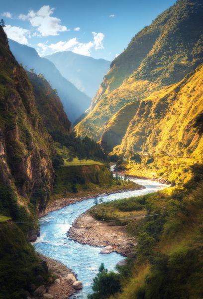 چشم انداز شگفت انگیز با کوه های Himalayan بالا رودخانه زیبا انحنا جنگل سبز آسمان آبی با ابرها و نور خورشید زرد در پاییز در نپال دره کوهستانی سفر در هیمالیا طبیعت