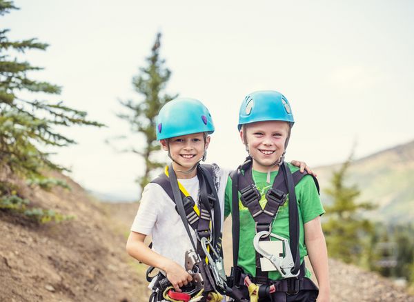 دو بچه خندان آماده برای رفتن به یک ماجراجویی خط فشرده در کوه ها در حالی که در یک تعطیلات تابستانی با هم با استفاده از کلاه ایمنی و داشتن یک زمان عالی