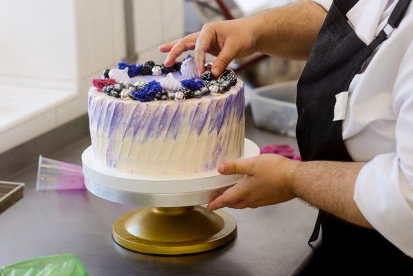 ساخت یک کیک زیبا بیکر توت های تزئینی را در بالای صفحه قرار می دهد کیک های پخت و تزئین برای عروسی تولد و یا هر رویداد