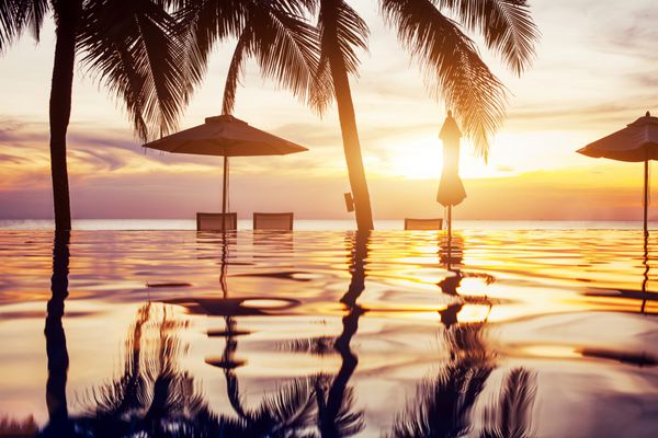استخر شنا ساحل در غروب آفتاب با بازتاب درختان نخل چشم انداز استوایی هتل جزیره ای عجیب و غریب