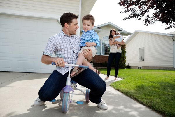 پدر بازیگوش بر روی سه چرخه نشسته با پسر و همسر ایستاده در پس زمینه با دختر