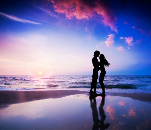 زن و شوهر رمانتیک در مورد بوسه در ساحل در غروب آفتاب