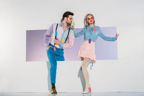 زن و شوهر جوان شیک با برچسب های رنگارنگ روی لباس هایی که از طریق باز کردن روی خاکستری می روند