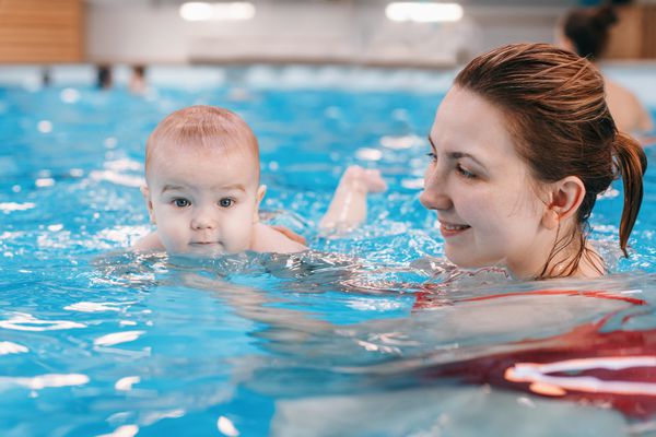 مادر قفقازی سفید کودک تازه متولد شده خود را برای شنا در استخر شنا می کند غواصی کودک در آب سبک زندگی فعال سالم فعالیت خانوادگی و مفهوم رشد اولیه