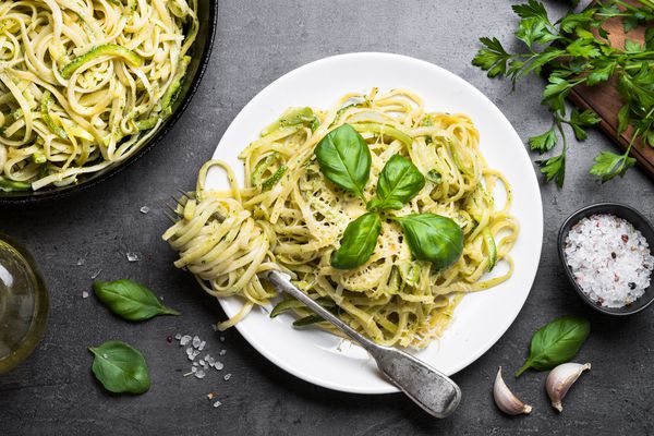 ماکارونی اسپاگتی با کدو ریحان خامه و پنیر روی میز سنگ سیاه قرار دارد ماکارونی سبزیجات گیاهی رشته فرنگی کدو سبز نمای بالا