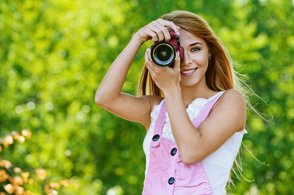 پرتره زن جوان و خندان با دوربین در مقابل فضای سبز پارک تابستان