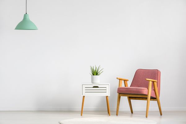 صندلی صورتی و میز چوبی روی دیوار خالی در فضای داخلی اتاق نشیمن ساده