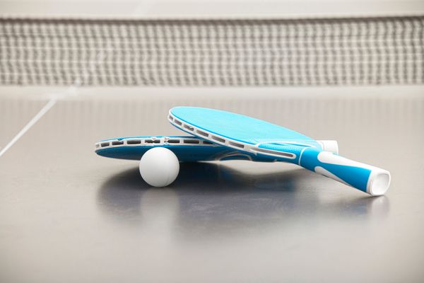 راکت های آبی برای تنیس که روی میز خاکستری با توپ سفید کوچک قرار دارند