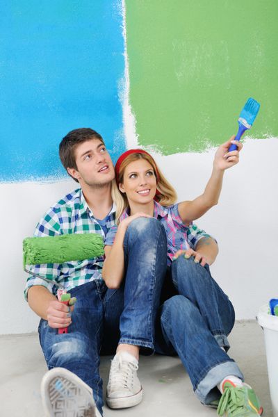 زن و شوهر جوان خوشبختی با دیوارهای سفید و رنگی سفید رنگ خانه جدیدشان نقاشی می کنند