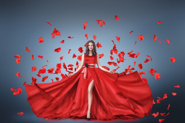 پرتره مد زن جوان در لباس قرمز بلند با گلبرگهای پرواز