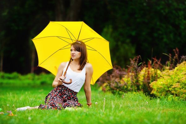 زن جوان زیبا در یک پارک با چتر