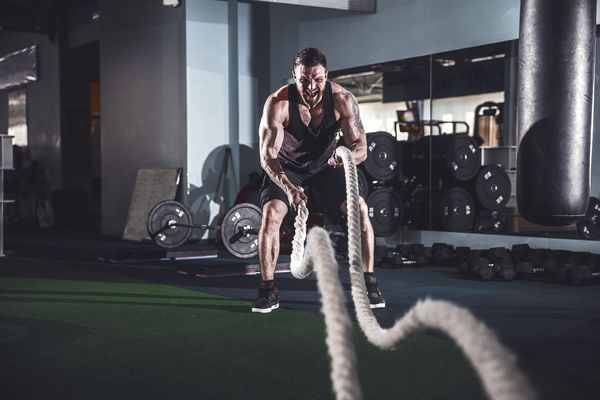 تمرینات مرد پرخاشگر قدرتمند عضلانی با طناب در سالن بدن سازی آموزش عملکردی