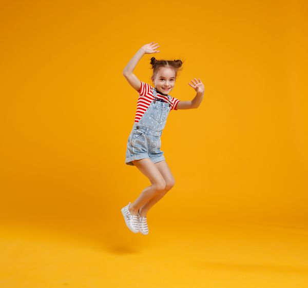 دختر کودک خنده دار پرش به یک پس زمینه زرد رنگی