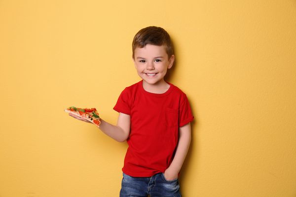 پسر بچه ناز با برش پیتزا در زمینه رنگی
