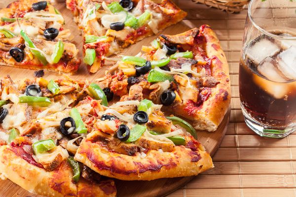 پیتزا با ژیروی مرغ فلفل سبز زیتون و پیاز روی تخته برش با کولا سرو شده است