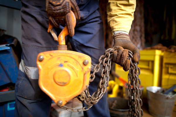 کارگر پرخطر Rigger با پوشیدن دستکش سنگین انجام بازرسی از سنگین زنجیره بلند کردن 3 تن که قبلاً در سایت معدن ساختمانی شهر پرت استرالیا استفاده می شد