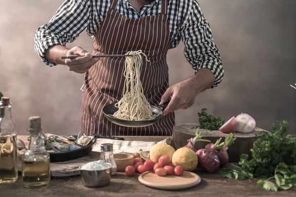 سرآشپز خوشبو ریش خوش تیپ که پیش از تهیه اسپاگتی روی آشپزخانه است سرآشپز آشپز را میل می کند